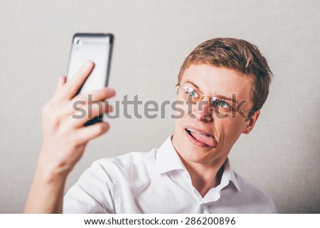 The man in glasses makes a Selfe jokingly phone. On a gray background.