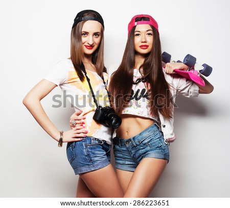 Two girl skaters go crazy and have fun together. Beautiful sporty women, positive emotion. Grey background.