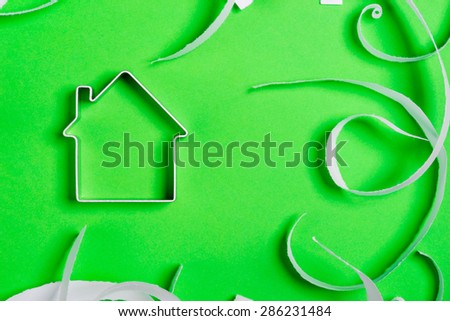 Funny metal house standing on a green surface with teared paper pieces