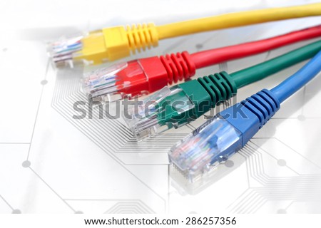 Four Multi Colored Network Cables. Red, Yellow, Green, Blue Color. Cables are lying on top of White Circuit Board
