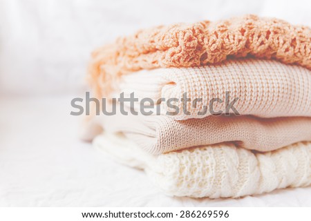 Pile of beige woolen clothes on a white background. Warm knitted sweaters and scarfs are folded in one heap. Imitation of Instagram style tone.