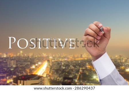 Business man's hand writing massage Positive at transparent board on blurred night city background