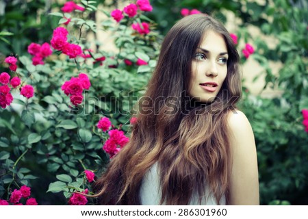 Beautiful brunette woman in blooming rose flowers. Outdoor portrait. Woman in spring park