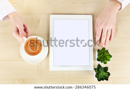 Hands with tablet and cup of coffee, on wooden table