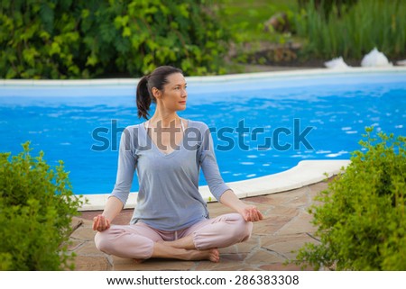 beautiful adult woman doing yoga on the shore of the pond