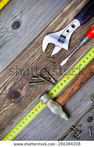 old screwdriver, screws, monkey wrench, vintage hammer and tape-measure on the boards of the old workbench
