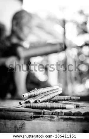Ready for silk weaving with spool of silk in thailand on black and white color,Focus on spool and Blurry on weaver background