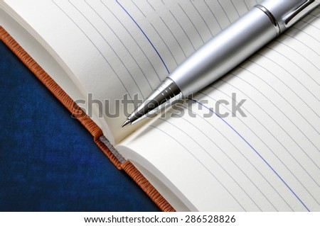 Silver metal pen on the opened notebook on blue background. Close-up.