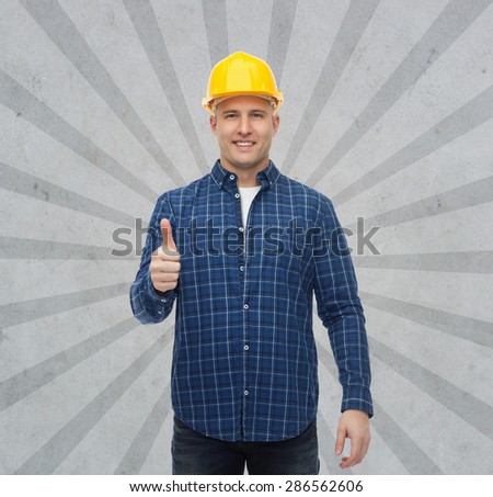 repair, construction, building, people and maintenance concept - smiling male builder or manual worker in helmet showing thumbs up over gray burst rays background
