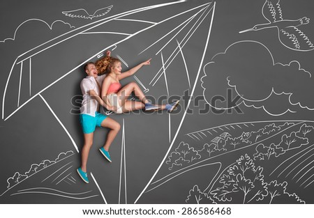 Happy valentines love story concept of a romantic couple on chalk drawings background. Couple on a date hang gliding over a countryside, female pointing at the flying duck.