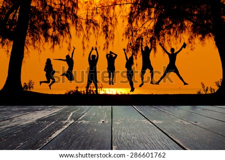 Wooden walkway and silhouette of friends jumping on beach