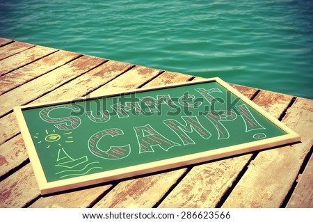 the text summer camp written with chalk of different colors in a chalkboard, on a wooden pier on the sea, slight vignette added