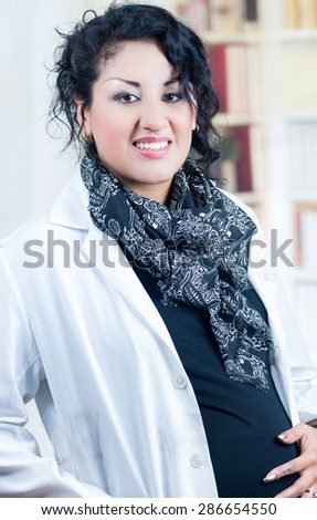pregnant woman wearing casual clothes and lab coat looking to camera with smile