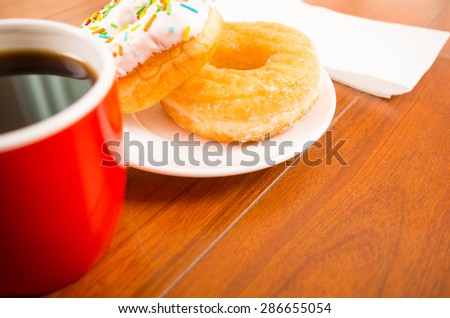 colorful donuts on a plate next to coffee cup and napkin from side angle