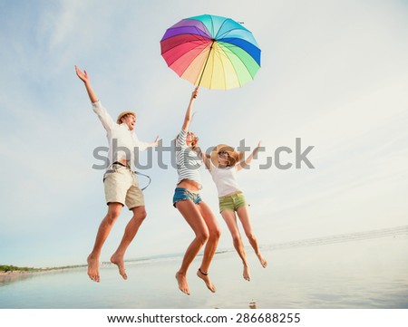 Group of happy young people having fun jumping with rainbow umbrella on the beach on bali