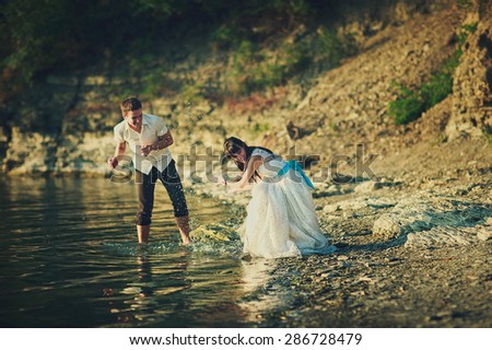 a happy just married couple is walking down the beach and splashing with water
