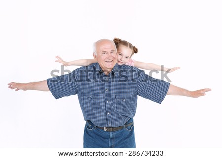 Portrait of a grandfather wearing blue checkered shirt standing and his small pretty granddaughter on his back pretending they are airplanes, isolated on a white background