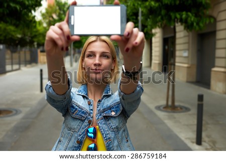 Young female holding smart phone with blank copy space area for your text message or content, tourist woman making self portrait with mobile phone digital camera during her vacation holidays in summer