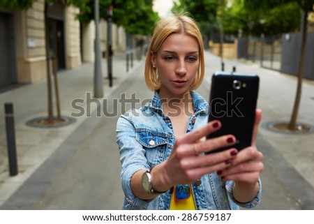 Stylish young woman photographing urban view with mobile phone camera during summer journey,gorgeous female tourist taking picture with her smart phone while standing outdoors in urban setting  street
