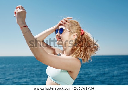 Happy fitness selfie blonde asian girl smiling and taking self portrait photograph with smart phone after running exercise workout on beach.