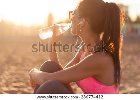Beautiful fitness athlete woman drinking water after work out exercising on sunset evening summer in beach outdoor portrait Royalty-Free Stock Photo #286774412