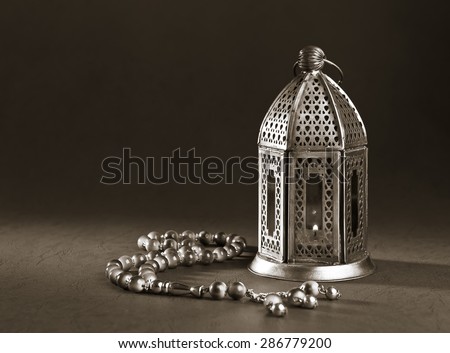 A metallic Ramadan lamp with Islamic rosary beads on black background. Monochromatic image. Royalty-Free Stock Photo #286779200