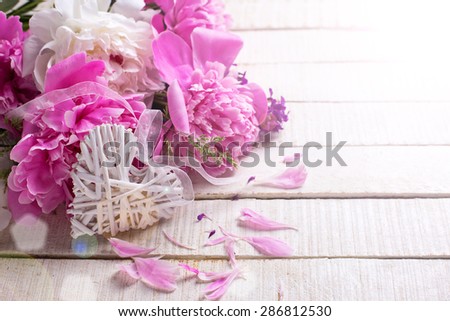 Decorative heart and fresh pink and white peonies flowers in ray of light  on white painted wooden planks. Selective focus. Place for text.