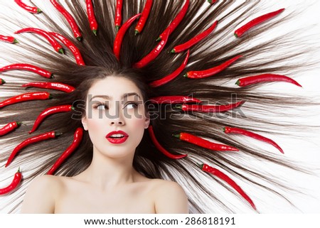 Closeup portrait of beautiful young woman lying with red chilli peppers in hair. Isolated on white background.