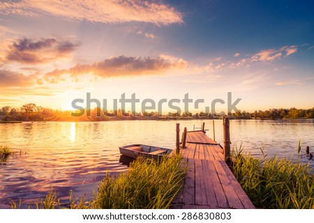 Sunset over the lake in the village. View from a wooden bridge, image in the orange-purple toning Royalty-Free Stock Photo #286830803