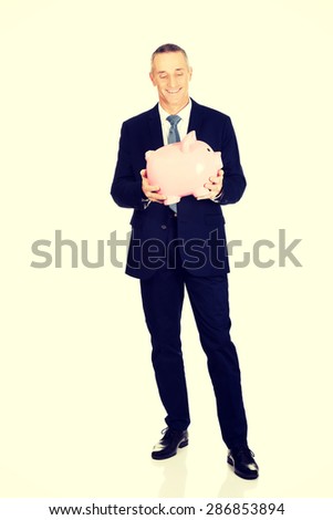 Full length cheerful businessman holding piggybank.