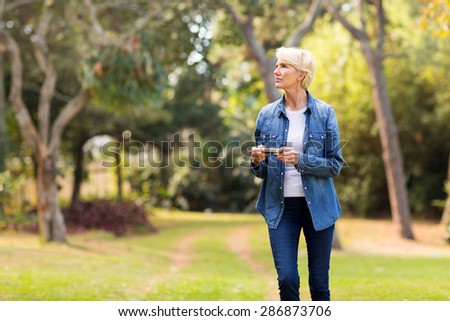 thoughtful middle aged woman holding camera outdoors