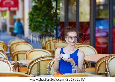 Beautiful young Parisian woman in blue tube top drinking coffee in an outdoor cafe on a summer day