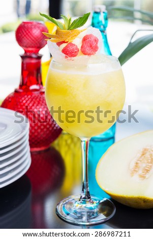 refreshing glass of bright juicy melon smoothie or lemonade with ice on a table at a restaurant with the decor of the bright dishes and pieces of melon