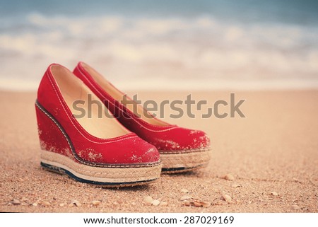red summer shoes standing on sandy ocean beach. vintage picture