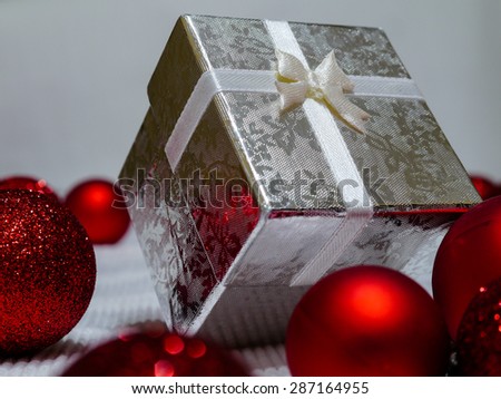 one silver gift box with crossed ribbon and lace or bow tie is on white surface next to ball decorations of glittered and brilliant texture special composition for celebration xmas evening in december
