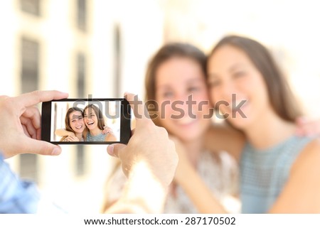 Blurred friends taking photos with a smart phone and showing the photo in the screen on the street