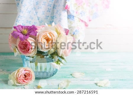Pink roses and violet clematis flowers  in vase  in ray of light on turquoise wooden background. Place for text. Selective focus. 