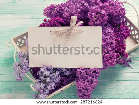 Fresh splendid lilac flowers on tray and empty tag on turquoise painted wooden planks. Selective focus. Place for text. Toned image.