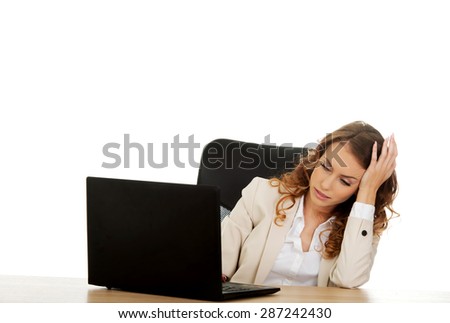 Tired businesswoman working on laptop by a desk.