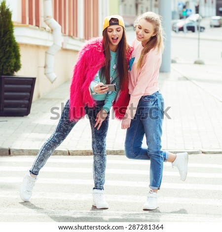 Hipster girlfriends taking a selfie in urban city context.