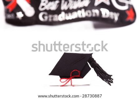 small cap and diploma with decorative ribbon in the background.  Focus on the cap and diploma