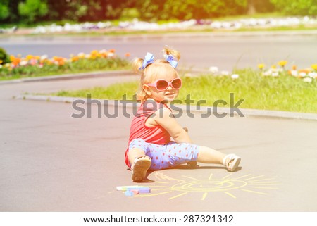cute little girl drawing sun with chalks on a street