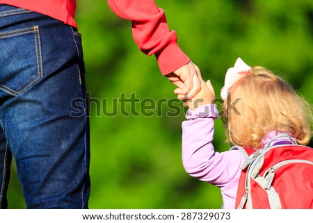 Mother holding hand of little daughter with backpack outdoors