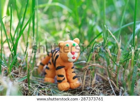 Plasticine world - little homemade orange tiger on a grass background , selective focus and place for text