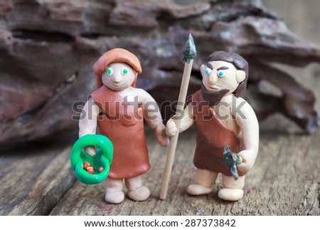 Plasticine world - a caveman with a spear and a stone ax and cave woman with a basket and berries, selective focus