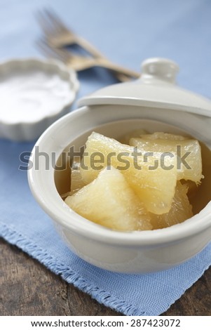 cooked casava or yucca in syrup serve with tiny cup of coconut milk. thai desseert. thai dessert in thai style bowl on cotton blue cloth on old wooden table. 
