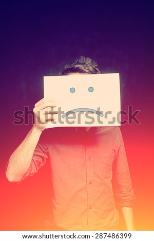 Young man with an unhappy smiley card covering face