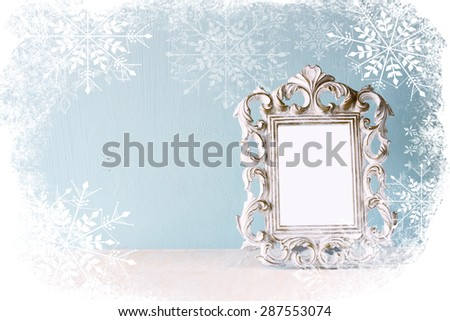abstract image of vintage antique classical frame on wooden table with snowflakes overlay