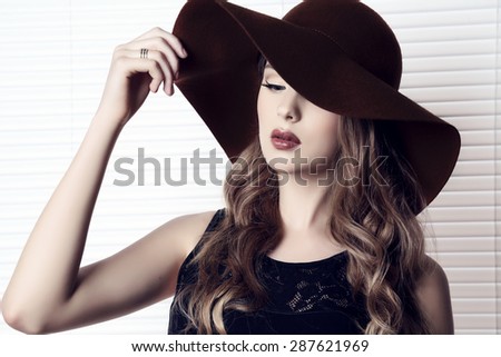 fashion studio photo of beautiful young girl with dark natural hair wearing black dress and elegant hat 