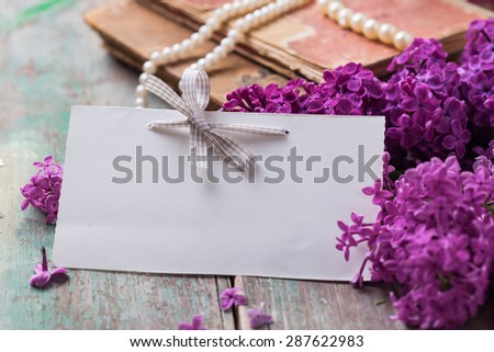 Postcard with  lilac flowers and empty tag for your text on aged wooden background. Selective focus is on tag.